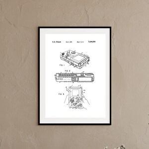 May include: A framed black and white print of a U.S. Patent document, number 5,184,830, dated Feb. 9, 1993. The technical illustration displays three distinct line drawings of a handheld electronic gaming device, labelled Fig. 1, Fig. 2, and Fig. 3.