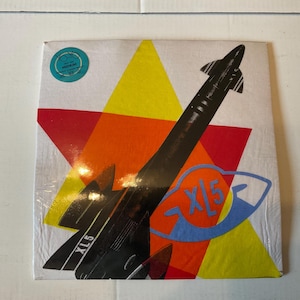 May include: A vintage vinyl record album cover featuring a black rocket ship design against a backdrop of red, yellow, and orange geometric shapes. The text "XL5" is visible on the rocket and the album title.