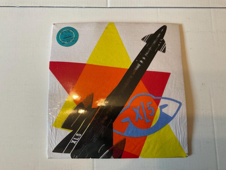 May include: A vintage vinyl record album cover featuring a black rocket ship design against a backdrop of red, yellow, and orange geometric shapes. The text "XL5" is visible on the rocket and the album title.