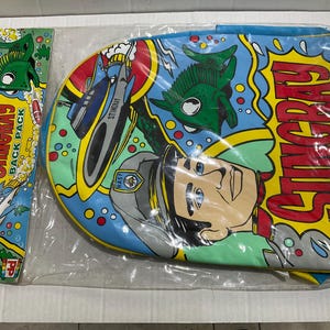 May include: A vintage Stingray backpack and pencil case set. The backpack is blue with a comic book style design featuring a cartoon character, a submarine, and the word "STINGRAY" in large yellow letters. The pencil case has a green fish design.