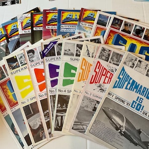 May include: A collection of vintage "Supermarionation" comic books. The covers feature bold colors, including red, yellow, blue, and green, with the series title prominently displayed. Some issues have images of characters and the text "Supermarionation is Go!"
