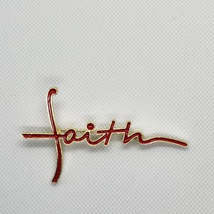 Puede incluir: Un pin de tono dorado con la palabra "fe" escrita en letras cursivas rojas. El pin presenta un dise&ntilde;o de cruz.
