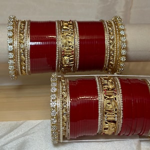 Può includere: Un set di braccialetti rossi e dorati con pietre bianche e trasparenti. I braccialetti sono decorati con disegni intricati e sono perfetti per un'occasione speciale.