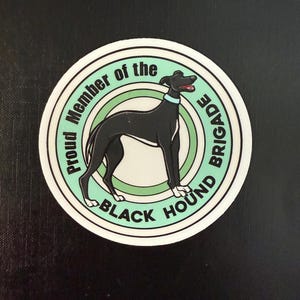 Puede incluir: Una pegatina circular blanca con una ilustración en blanco y negro de un perro. La pegatina dice "Proud Member of the Black Hound Brigade" en un círculo verde.