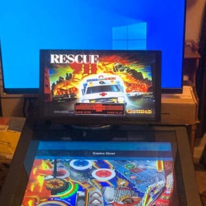 May include: A pinball machine with a digital display showing "Game Over" and "Final Score". The game is Rescue 911 and the screen shows a white ambulance with a red cross.
