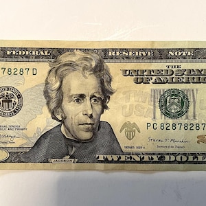 May include: A twenty-dollar bill featuring a portrait of Andrew Jackson. The bill is primarily green and tan, with the text "The United States of America" and "Twenty Dollars" visible.