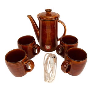 May include: A brown ceramic coffee set with a matching teapot, four mugs, and a white electrical cord. The set has a textured finish and a classic design, perfect for serving coffee or tea.