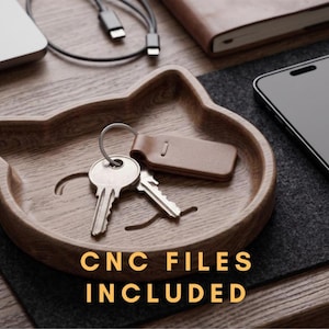 May include: A wooden tray shaped like a cat head with two pointed ears, featuring engraved whiskers and a smooth finish. Inside the tray are two metal keys on a ring with a brown leather tag. The text CNC FILES INCLUDED is printed in yellow.