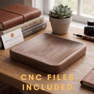 Può includere: Un vassoio quadrato in legno con bordi arrotondati, realizzato in legno scuro con venature visibili, è appoggiato su una superficie di legno. Il testo "CNC FILES INCLUDED" è visualizzato in oro. Altri elementi includono libri, una succulenta e una penna.