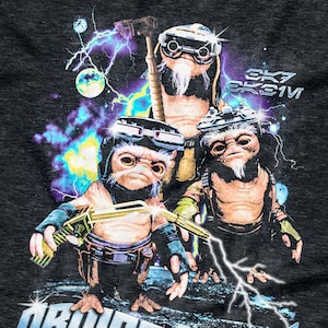May include: Dark grey t-shirt with a vibrant graphic of three alien figures in futuristic attire, set against a backdrop of lightning and planets. The text "DROIDSMITHS" is displayed in a stylized font below the figures.