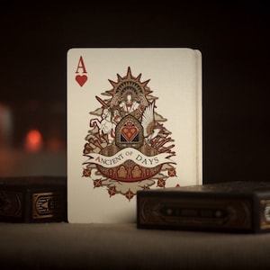May include: A playing card from the Ancient of Days deck. The card is the Ace of Hearts and features an intricate design with a winged figure and a banner that reads "Ancient of Days".