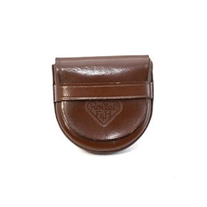 Puede incluir: Una funda de cámara de cuero marrón con base curva y cierre de solapa. La funda tiene una correa en la parte delantera y el logotipo de Rollei en relieve. La funda está diseñada para proteger una cámara.