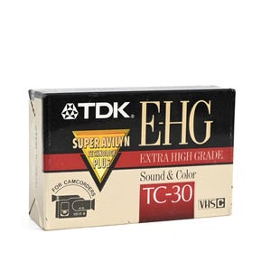 Könnte beinhalten: Eine TDK EHG TC-30 VHS-C Videokassettenbox. Die Box ist schwarz, beige und rot mit dem Text "SUPER AVILYN TECHNOLOGY PLUS" und "EXTRA HIGH GRADE". Sie hat auch den Text "Sound & Color" und "TC-30".