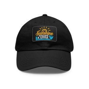 May include: Black baseball cap with a patch that says "Sunshine mixed with a little hurricane" in yellow and blue text.
