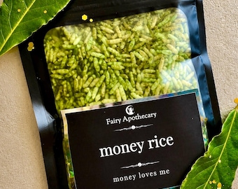May include: A black resealable pouch containing green-tinted rice grains. The label features the text Fairy Apothecary, money rice, and money loves me in white font. Two green leaves with gold glitter accents are positioned on the sides.