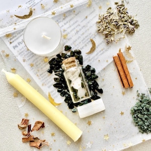May include: A Pet Protection Spell Jar kit containing a small glass bottle with a cork stopper, a white tea light candle, a yellow taper candle, dried lavender, two cinnamon sticks, green stone chips, and a white crystal wand in a gold star mesh bag.