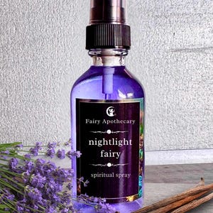 May include: A purple glass bottle of "nightlight fairy spiritual spray" with a black label, a clear spray top, and a black cap. The bottle is next to a bundle of lavender and several vanilla beans.