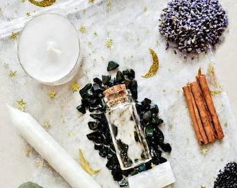 May include: A small glass bottle with a cork stopper filled with white contents, surrounded by dark green stone chips, a white taper candle, a white tea light, dried lavender, cinnamon sticks, black salt, and eucalyptus leaves.