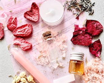 May include: A pink organza bag with gold star prints containing a white tea light candle, a small glass vial with a cork, a small amber bottle with a silver cap, a pink taper candle, pink salt crystals, dried red rose petals, and dried flowers.