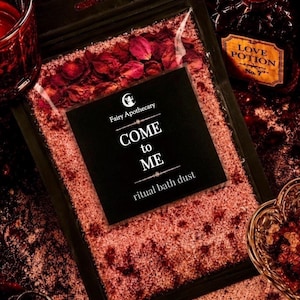 May include: A clear plastic pouch filled with pink bath salts and dried red rose petals. A black label features the text Fairy Apothecary, COME to ME, and ritual bath dust. The pouch is surrounded by a red glass candle and a bottle labeled Love Potion.