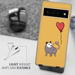 Puede incluir: Una funda de tel&eacute;fono amarilla con un opossum de dibujos animados sosteniendo un globo rojo en forma de coraz&oacute;n. La funda tiene un recorte para la c&aacute;mara y el texto "LIGHT WEIGHT SOFT AND FLEXIBLE" en la parte inferior.