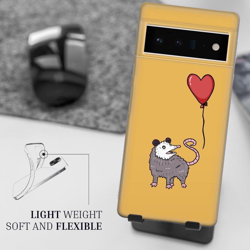 Puede incluir: Una funda de tel&eacute;fono amarilla con un opossum de dibujos animados sosteniendo un globo rojo en forma de coraz&oacute;n. La funda tiene un recorte para la c&aacute;mara y el texto "LIGHT WEIGHT SOFT AND FLEXIBLE" en la parte inferior.