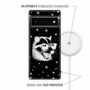 Puede incluir: Una funda de tel&eacute;fono negra con una ilustraci&oacute;n blanca de un mapache con gafas de sol sobre un fondo negro con estrellas blancas. La funda admite carga inal&aacute;mbrica. El texto "SUPPORTS WIRELESS CHARGING" y "SIDES ARE NOT PRINTED" est&aacute; impreso en la imagen.