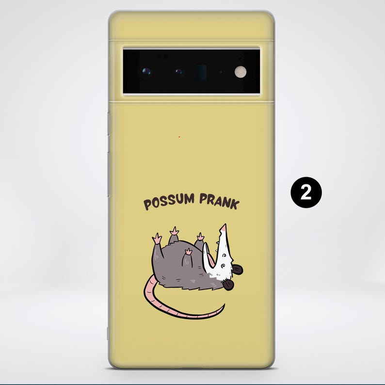 Puede incluir: Una funda de tel&eacute;fono amarilla con un opossum de dibujos animados en ella. El opossum est&aacute; tumbado de espaldas con las patas en el aire. El texto "Possum Prank" est&aacute; impreso en la funda.