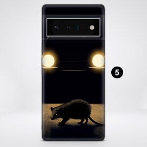 Puede incluir: Una funda de tel&eacute;fono negra con un gr&aacute;fico de un coche con los faros encendidos y un peque&ntilde;o animal en primer plano.