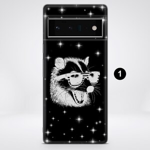 Puede incluir: Carcasa de tel&eacute;fono negra con una ilustraci&oacute;n blanca de un mapache con gafas de sol sobre un fondo negro con estrellas blancas.