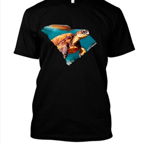 May include: Black t-shirt featuring a colorful illustration of a sea turtle within the outline of South Carolina. The turtle is depicted in shades of brown, orange, and yellow, swimming in blue water. The text "SOUTH CAROLINA" is printed on the design.