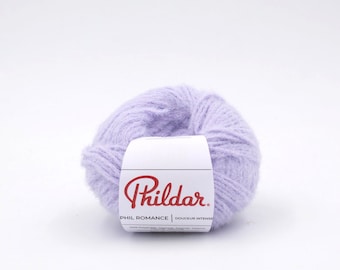 Peut inclure: Un peloton de fil de couleur lavande avec une étiquette blanche sur laquelle est inscrit "Phildar. PHIL ROMANCE | DOUCEUR INTENSE"