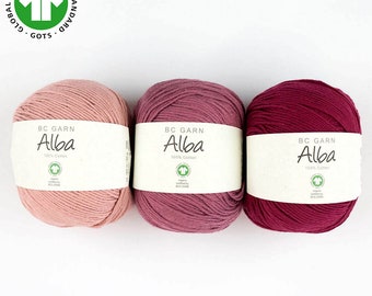 May include: Three balls of yarn in shades of pink, rose, and burgundy. Each ball is labeled "BC Garn Alba 100% Cotton" and features a green GOTS logo.