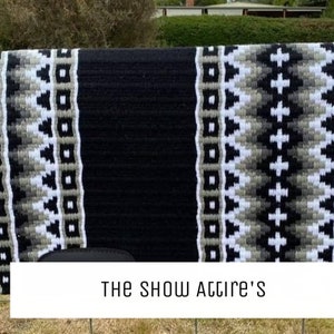 May include: Black and white saddle pad with a geometric pattern. The saddle pad has a black center with white and gray borders. The text "THE SHOW ATTIRE'S" is printed on the bottom of the saddle pad.