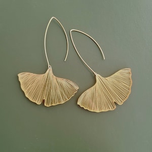 May include: A pair of gold-tone earrings shaped like ginkgo leaves. The leaves are delicate and have a wire-like design.