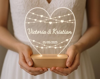 May include: A heart-shaped LED light with the names "Victoria & Kristian" and the date 05/05/2025 etched on the surface. The light is supported by a wooden base and features strings of hearts.
