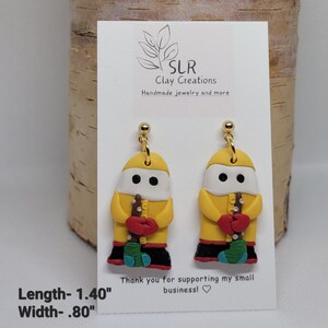 May include: Yellow clay earrings shaped like a person wearing a yellow raincoat and holding a red and green object. The earrings are 1.40 inches long and .80 inches wide. "SLR Clay Creations Handmade jewelry and more" and "Thank you for supporting my small business!" are written on the card.