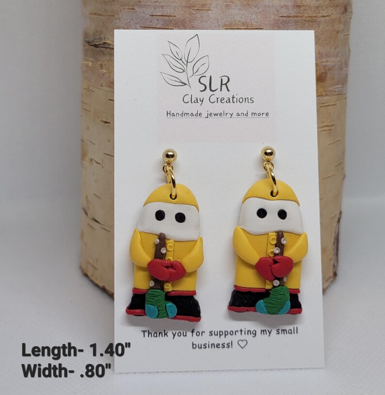 May include: Yellow clay earrings shaped like a person wearing a yellow raincoat and holding a red and green object. The earrings are 1.40 inches long and .80 inches wide. "SLR Clay Creations Handmade jewelry and more" and "Thank you for supporting my small business!" are written on the card.