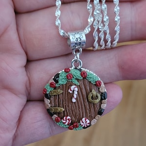 May include: A silver chain necklace with a round pendant featuring a brown wooden door with a candy cane, red and white candy, and green holly leaves.