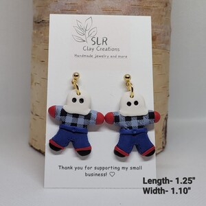 May include: A pair of handmade polymer clay earrings featuring a ghost wearing a blue and black plaid shirt and blue jeans. The earrings are approximately 1.25 inches long and 1.10 inches wide.