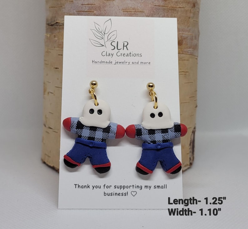 May include: A pair of handmade polymer clay earrings featuring a ghost wearing a blue and black plaid shirt and blue jeans. The earrings are approximately 1.25 inches long and 1.10 inches wide.