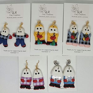 May include: Six pairs of handmade polymer clay earrings featuring a snowman design. Each pair features a different color scheme and pattern, including red, blue, yellow, white, and black. The earrings are all made with a white base and have a whimsical, cartoon-like style.