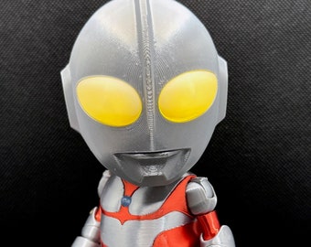 Puede incluir: Figura impresa en 3D de un personaje de estilo caricatura con cabeza plateada, torso rojo y extremidades plateadas. La figura tiene ojos amarillos grandes y una cresta distintiva en la cabeza. El texto en la imagen dice "2.0 FIGURE INCLUDES" y "Updated joints, articulation, colorway."