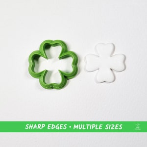 Può includere: Un tagliapasta in plastica verde a forma di trifoglio a quattro foglie con un ritaglio di pasta di zucchero bianca della stessa forma. "SHARP EDGES - MULTIPLE SIZES" è stampato su uno striscione verde sotto l'immagine.