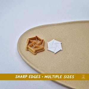Può includere: Due formine per biscotti a forma di stella, una beige e una bianca, sono su un piatto ovale beige. La formina beige è piena, mentre quella bianca ha un design aperto. Il testo in basso recita "SHARP EDGES • MULTIPLE SIZES."