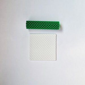 Può includere: Un oggetto cilindrico verde strutturato e un oggetto quadrato bianco con un motivo a scaglie sono mostrati su uno sfondo bianco. Sembrano essere materiali o strumenti per l'artigianato.