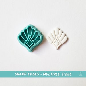 Op de afbeelding: Een turquoise plastic koekjessnijder en een witte fondant uitsteker, beide in een gestileerd bloemmotief. De uitsteker heeft een ruitvorm in het midden. De tekst onderaan luidt "SHARP EDGES • MULTIPLE SIZES."