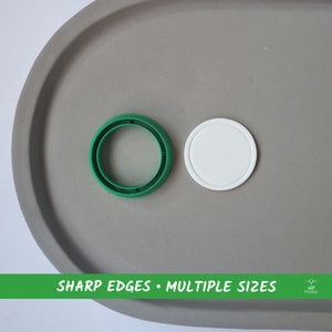 May include: Two round plastic lids, one green and one white. The green lid has a sharp edge and is slightly larger than the white lid. The lids are on a gray surface. "SHARP EDGES • MULTIPLE SIZES" is printed on a green banner at the bottom of the image.