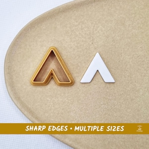 Puede incluir: Un cortador de galletas en forma de galón dorado con un borde elevado y una pieza de corte en forma de galón blanco a juego. La imagen incluye el texto SHARP EDGES • MULTIPLE SIZES en la parte inferior, indicando las características del producto.