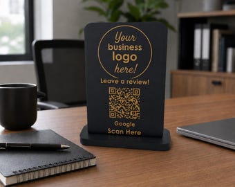 May include: A black rectangular sign with a gold base featuring the text Your business logo here! Leave a review! and Google Scan Here, along with a central QR code. The sign is designed for business display and customer interaction.
